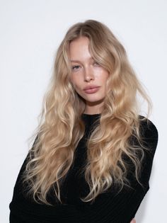 Blonde woman with long wavy hair and freckles wearing a black sweater