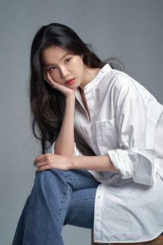 Woman with long dark hair wearing a white shirt and blue jeans in a studio