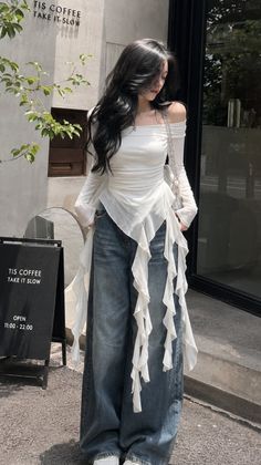 Woman with long black hair wearing an off-shoulder top and wide-leg jeans outdoors