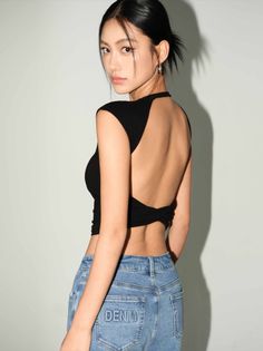 Woman in a black open-back top and blue jeans looking over her shoulder
