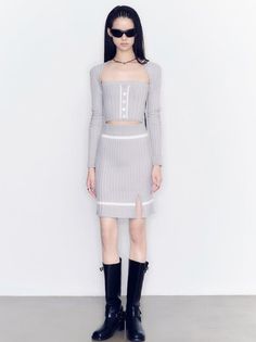 Woman in a gray ribbed knit crop top and mini skirt with black boots and sunglasses