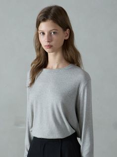 Woman with long brown hair wearing a grey long-sleeve shirt and black pants