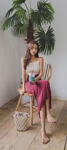 Woman with long hair in a sleeveless top and maxi skirt sitting on a wooden chair