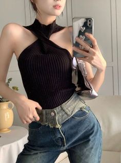 Woman in a black halter neck top and denim jeans taking a mirror selfie