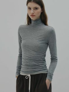 Woman in a gray turtleneck and brown pants posing in a studio