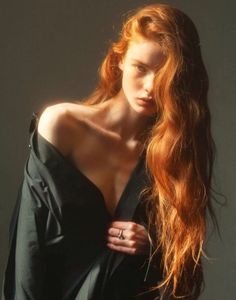 Woman with long red hair in a dark shirt with exposed shoulder and cleavage