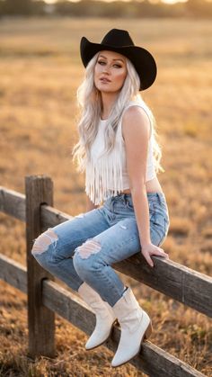 Woman in a cowboy hat and ripped jeans sitting on a wooden fence at golden hour