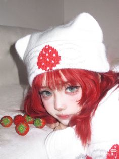 Person with bright red hair and a white beanie with a strawberry print