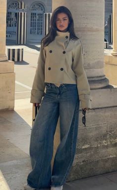 Woman in a cropped jacket and wide leg jeans leaning against a pillar outdoors
