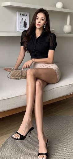 Woman with long hair wearing a black shirt and mini skirt, sitting indoors