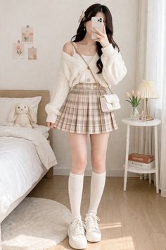 Woman in a plaid skirt and cardigan taking a mirror selfie in a bedroom