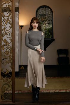 Woman with long hair in a gray top and long skirt standing indoors