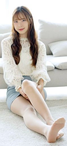 Woman with long hair wearing a white lace blouse and mini skirt, sitting indoors