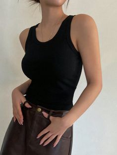 Person in a black tank top and brown pants with hands on hips