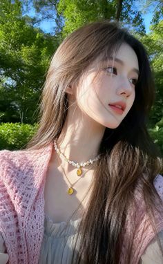 Woman with long hair wearing a pink cardigan and pearl necklace outdoors