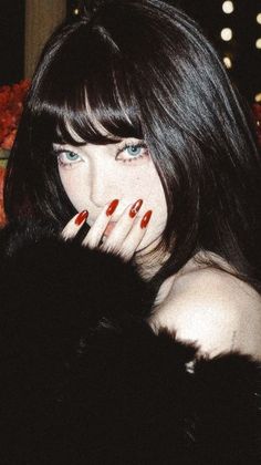 Woman with long black hair and blue eyes covering her mouth with a hand
