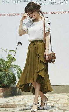Woman in a white blouse and olive ruffle skirt with a shoulder bag outdoors