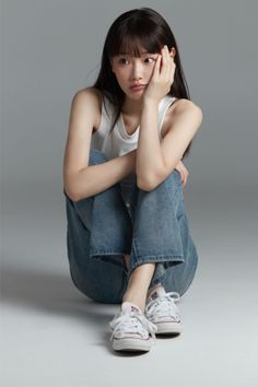 Woman with long hair and bangs wearing a white tank top and jeans, sitting on the floor