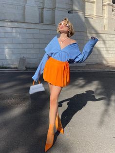 Woman in an orange skirt and blue shirt posing outdoors in bright sunlight