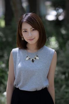 Woman with short brown hair wearing a gray top and necklace outdoors