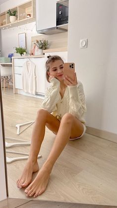 Woman in a white cable knit cardigan taking a mirror selfie indoors