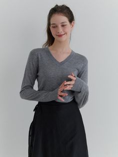 Woman in a gray v-neck sweater and black skirt with a ponytail indoors
