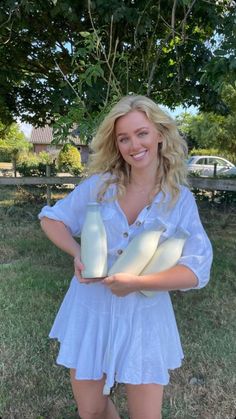 Blonde woman in a white dress holding bottles of milk outdoors