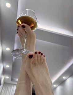 Feet with red nail polish holding a wine glass against a ceiling