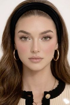 Woman with long brown hair and a black headband wearing gold hoop earrings