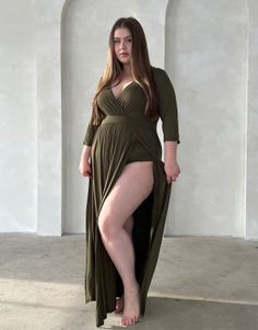 Woman in a green dress with a high slit and cleavage, standing indoors