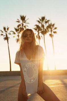 Woman in an oversized t-shirt and sunglasses at sunset with palm trees