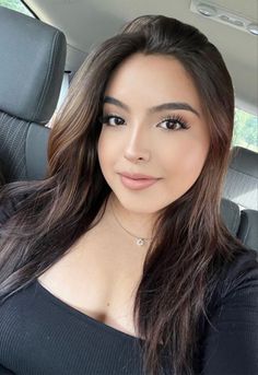 Woman with long dark hair wearing a black top and necklace in a car