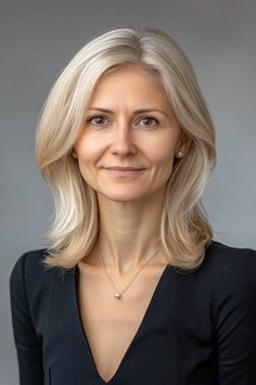 Woman with blonde hair wearing a black top and jewelry, smiling at the camera