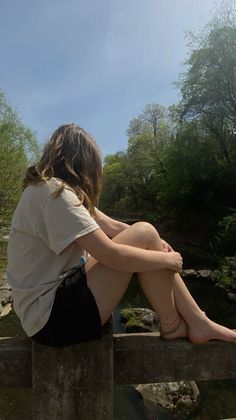Person with long hair sitting on a concrete ledge overlooking a stream