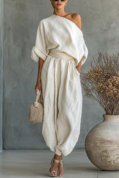 Woman in an off-shoulder top and harem pants holding a straw bag indoors