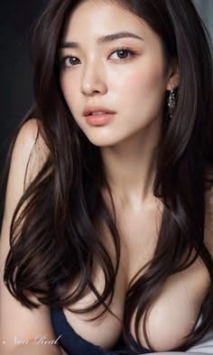 Woman with long dark hair and visible cleavage in soft lighting