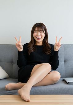 Woman in a black dress sitting on a couch making peace signs