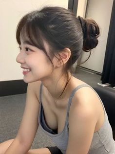 Woman with a messy bun and a grey tank top, smiling and showing cleavage