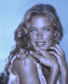 Woman with blonde curly hair and blue eyes smiling at the camera