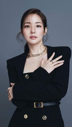 Woman in a black blazer and gold jewelry posing in a studio