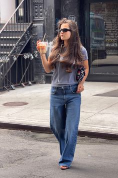 Woman with long hair and sunglasses walking on a street with a drink