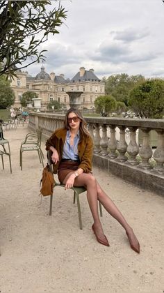 Woman in a brown jacket and mini skirt sitting on a chair in a park