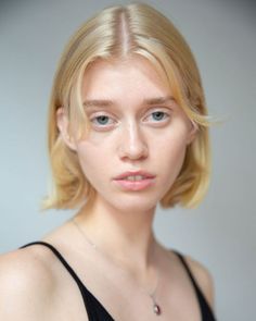 Woman with blonde short hair and blue eyes wearing a black top and silver necklace