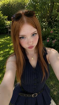 Young woman with red hair and freckles wearing a pinstripe dress and sunglasses on her head