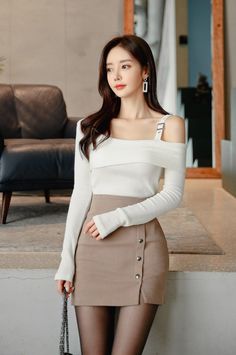 Woman with long dark hair wearing an off-shoulder top and mini skirt indoors