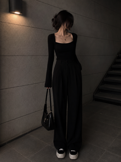 Woman in a black long sleeve top and wide leg pants holding a shoulder bag
