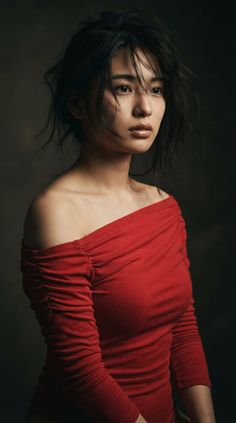 Woman in a red off-shoulder top with dark hair against a dark background