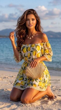 Woman in a lemon print dress kneeling on a beach at golden hour