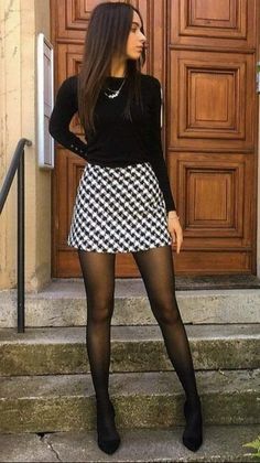 Woman in a black top and patterned mini skirt with tights standing outdoors