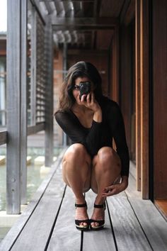 Woman with long hair squatting on a wooden deck, holding a camera